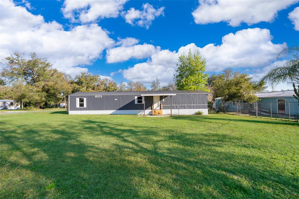 A single-story manufactured home with dark gray siding sits on a large, grassy lot — 101 CAROLINE AVENUE, LADY LAKE, FL