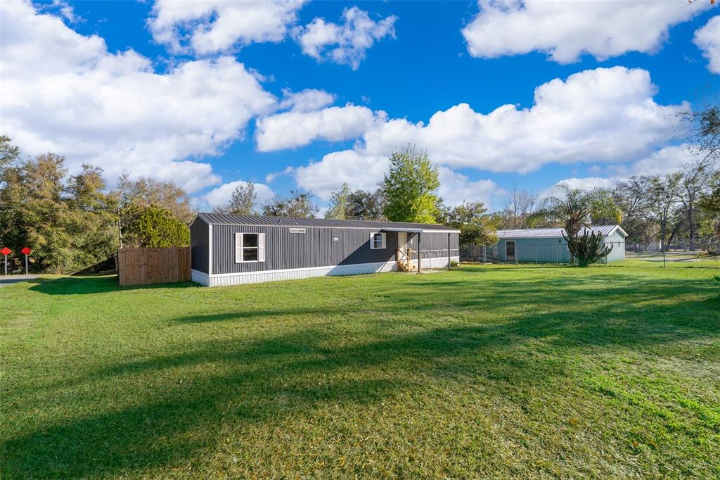 A dark gray mobile home sits on a large, grassy lot under a blue sky — 101 CAROLINE AVENUE, LADY LAKE, FL