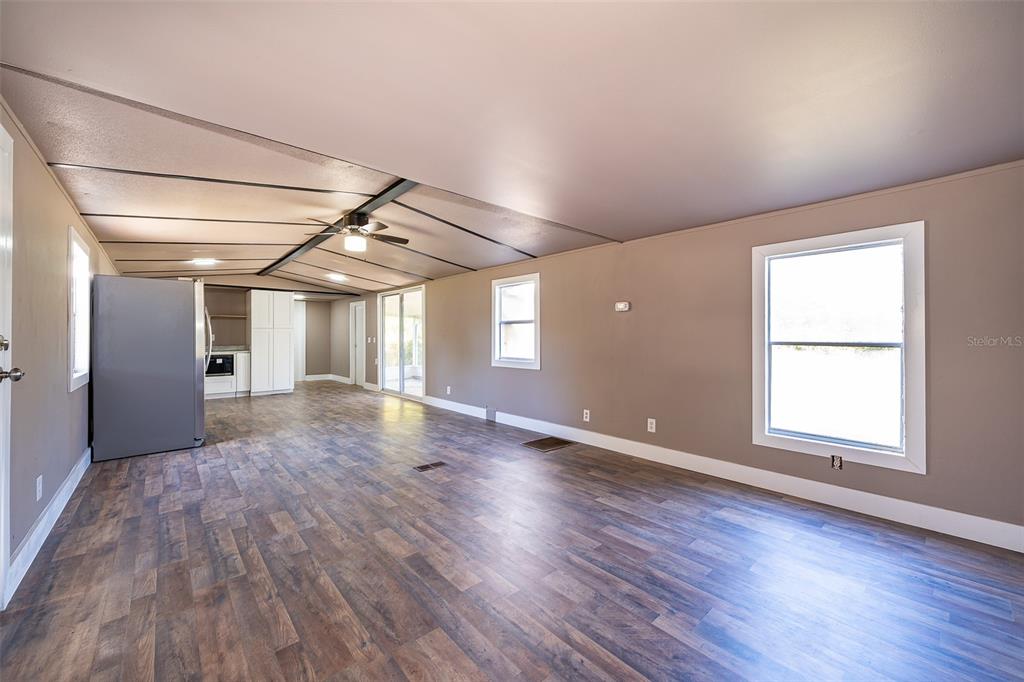 An open-concept living area features wood-look flooring, a ceiling fan, and a kitchen corner — 101 CAROLINE AVENUE, LADY LAKE, FL