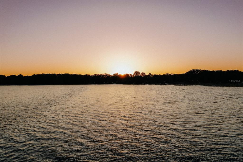 A sunset view over a calm lake with a treeline silhouette in the distance — 0 SE 202ND TER, HAWTHORNE, FL