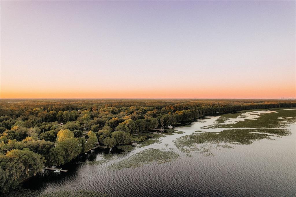 An aerial view shows a lake with lily pads bordered by a dense forest at sunset — 0 SE 202ND TER, HAWTHORNE, FL