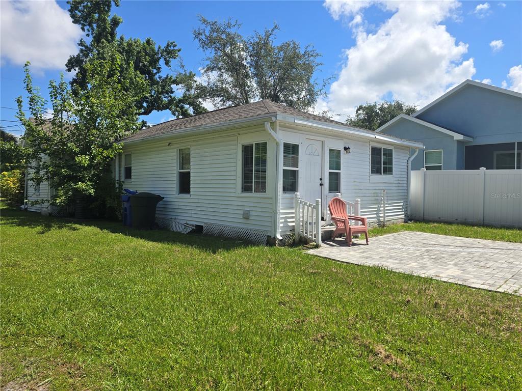 A white, single-story house exterior with a paved patio and a red plastic chair — 1327 GEORGIA AVENUE, DUNEDIN, FL