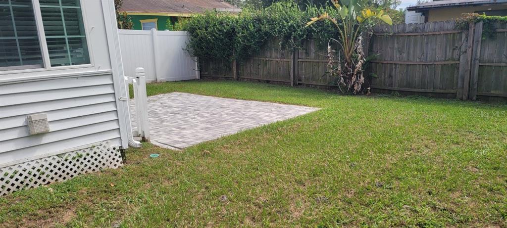 A backyard features a small paver patio, a white vinyl fence, and a wooden fence — 1327 GEORGIA AVENUE, DUNEDIN, FL