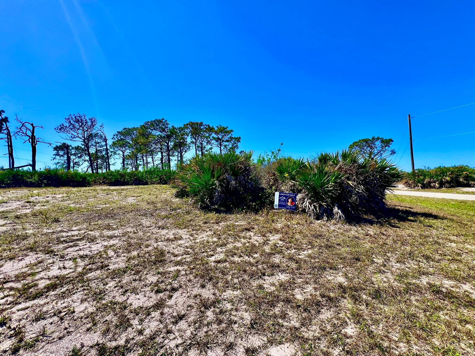 A vacant, sandy lot features scattered palmetto bushes and a small land for sale sign — 11 Boat Court, FL 33946, FL