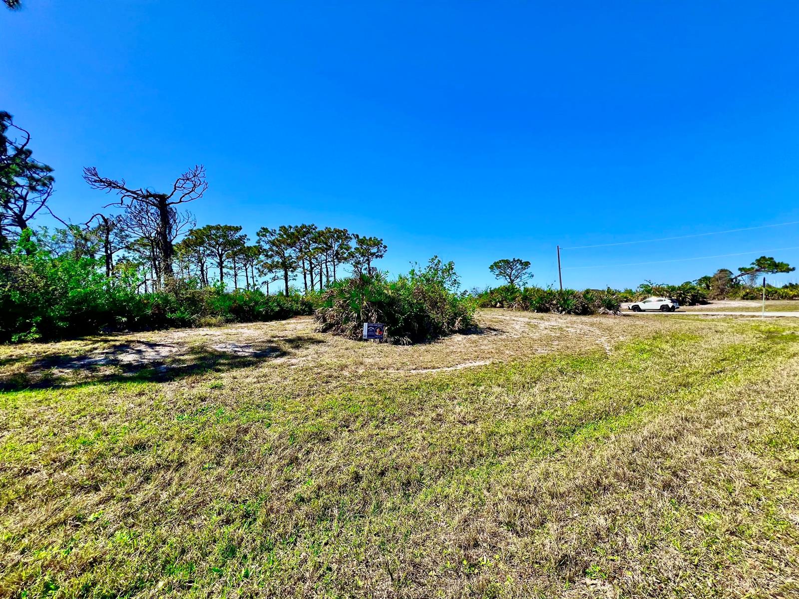 A vacant, grassy lot features scattered shrubs and a small for-sale sign under a blue sky — 11 Boat Court, FL 33946, FL