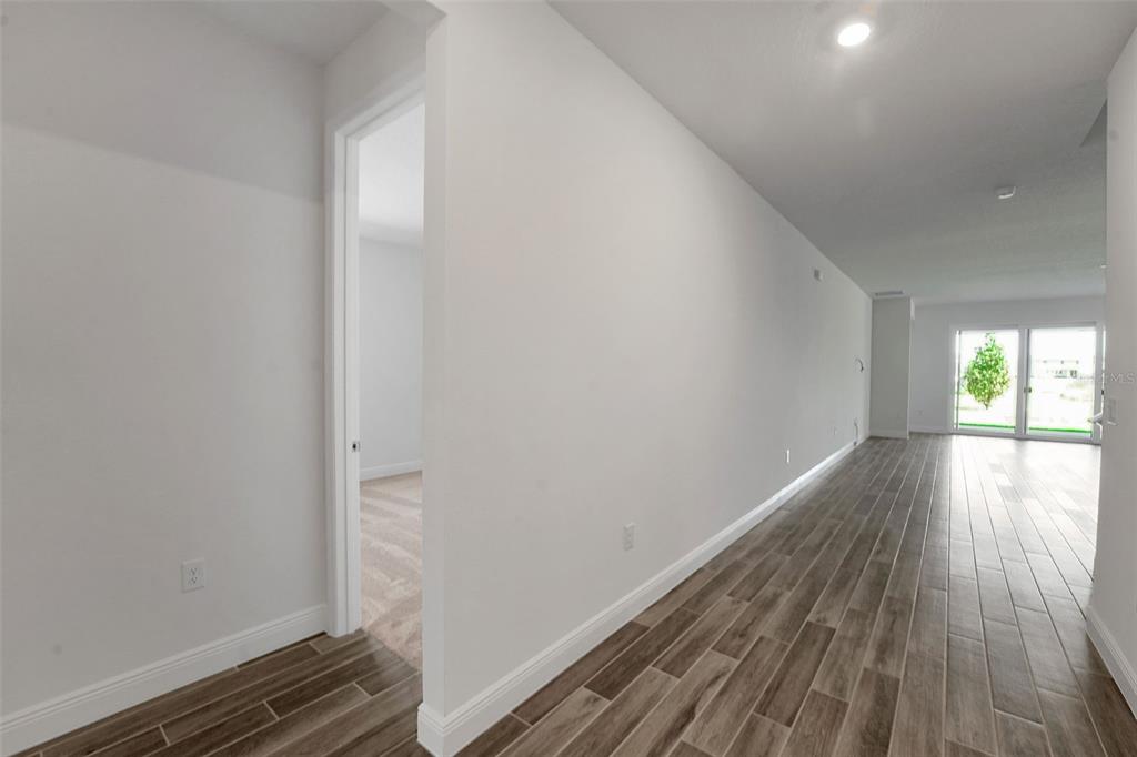 A hallway with wood-look tile flooring leads to a living area with sliding glass doors — 17546 VALLEYWOOD PARKWAY, LAND O LAKES, FL