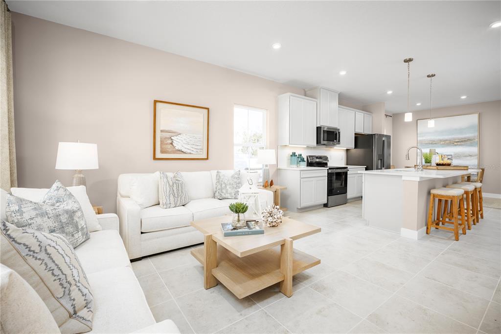 A bright open-concept living room and kitchen featuring white cabinetry and light tile flooring — 606 AVERYBECK LANE, DEBARY, FL