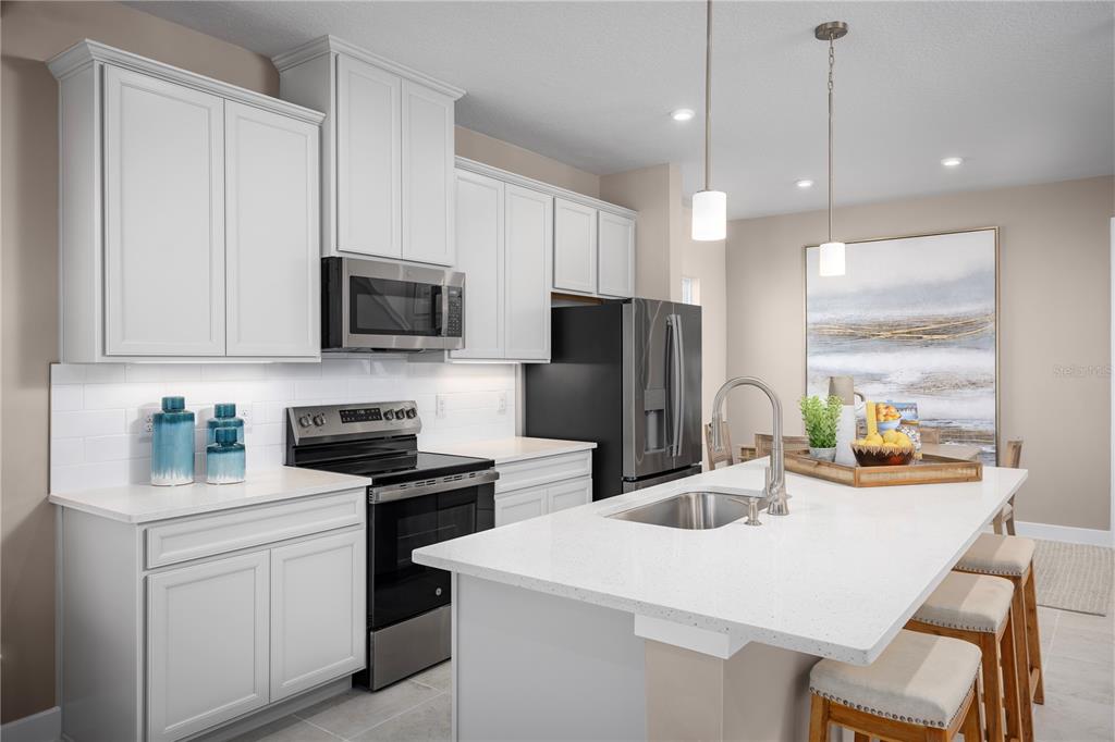 A modern kitchen features white cabinets, stainless steel appliances, a quartz island, and pendant lighting — 606 AVERYBECK LANE, DEBARY, FL