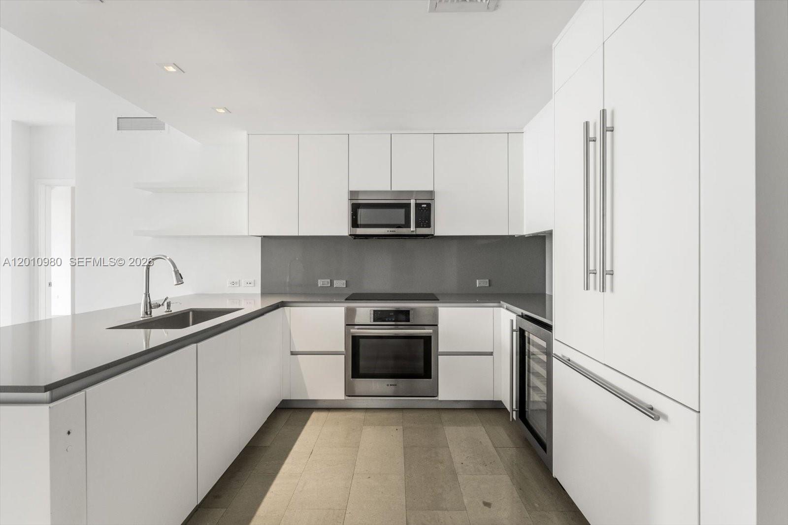 A modern kitchen features white cabinetry, stainless steel appliances, and gray countertops — 68 SE 6th St # 2304, Miami FL 33131, MIAMI, FL