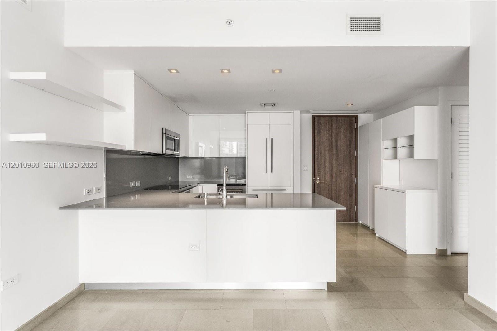 A modern kitchen features white cabinetry, a gray countertop island, and light tile flooring — 68 SE 6th St # 2304, Miami FL 33131, MIAMI, FL