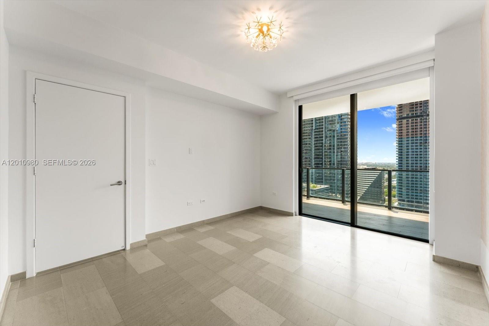 An empty room with light tile flooring, a white door, and a balcony overlooking skyscrapers — 68 SE 6th St # 2304, Miami FL 33131, MIAMI, FL