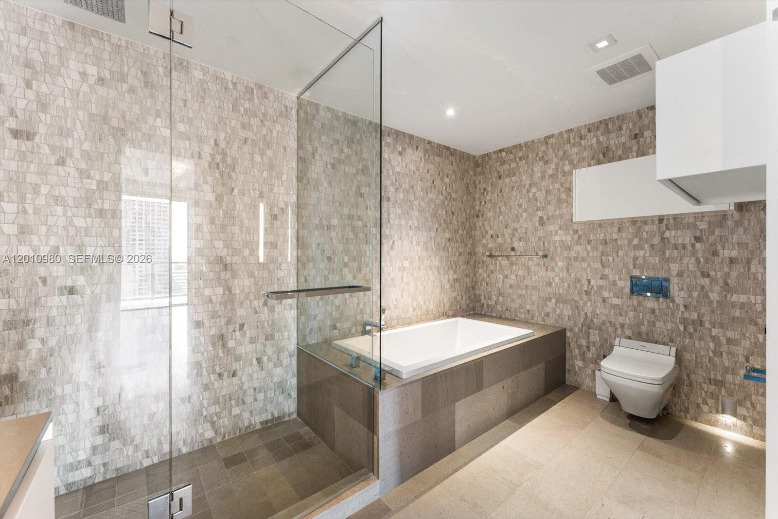 A modern bathroom features a glass-enclosed shower, a built-in bathtub, and neutral mosaic tile walls — 68 SE 6th St # 2304, Miami FL 33131, MIAMI, FL
