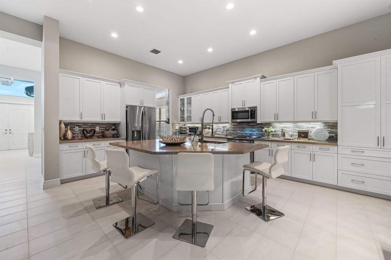 A modern kitchen features white cabinetry, a large central island with seating, and tile flooring — 12882 Granite Mountain Pass, Boynton Beach FL 33437, BOYNTON BEACH, FL