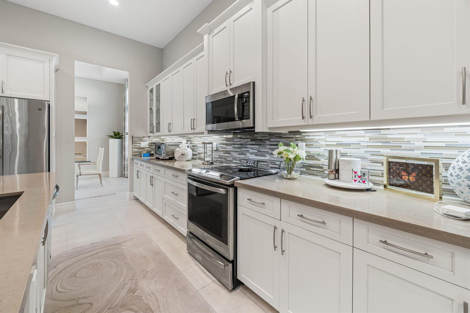 A kitchen features white cabinets, stainless steel appliances, quartz countertops, and a glass tile backsplash — 12882 Granite Mountain Pass, Boynton Beach FL 33437, BOYNTON BEACH, FL