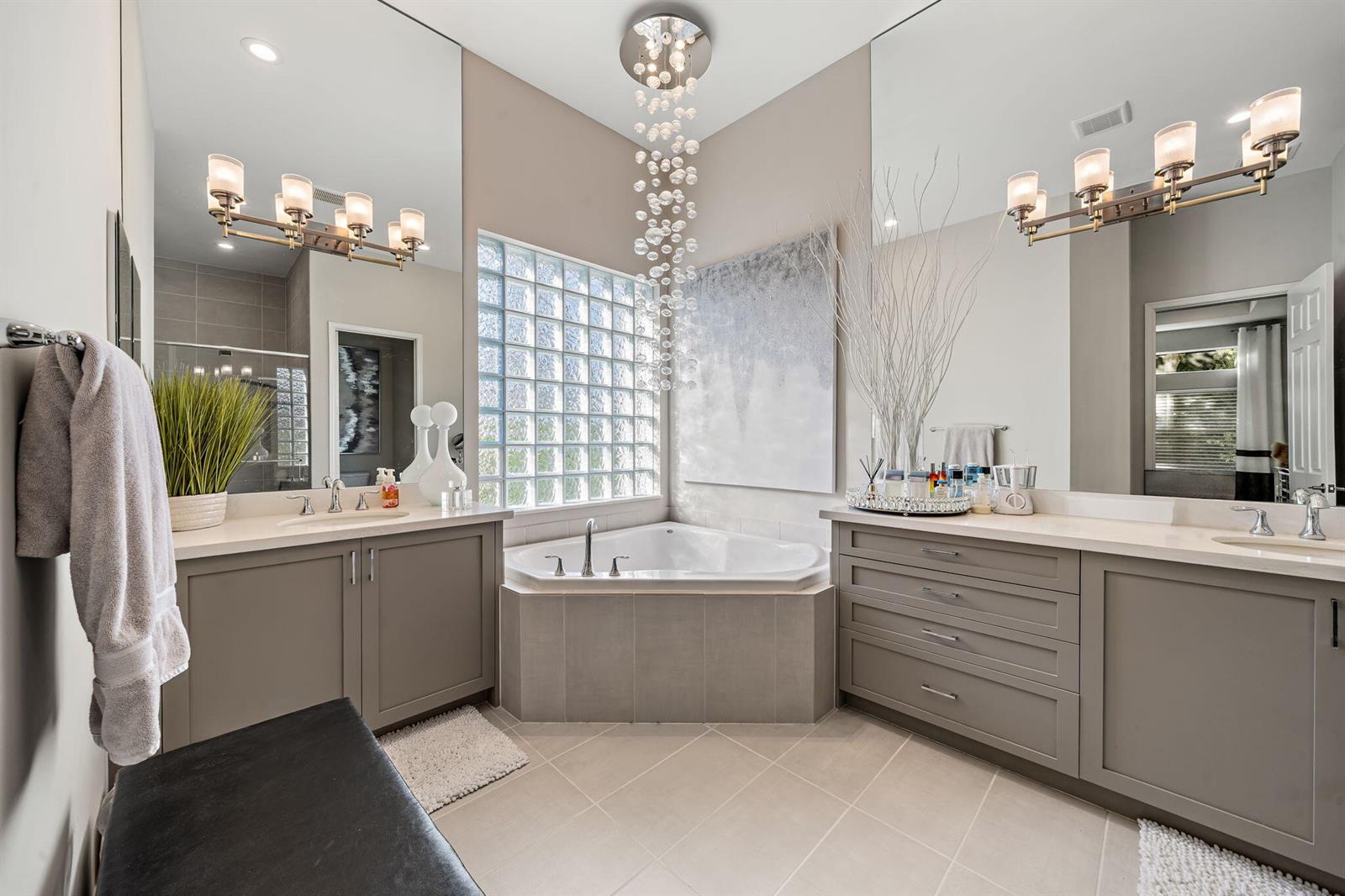 A bathroom features a corner soaking tub, dual vanities, glass block windows, and a crystal chandelier — 12882 Granite Mountain Pass, Boynton Beach FL 33437, BOYNTON BEACH, FL