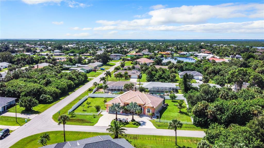 An aerial view shows a single-story house with a tiled roof surrounded by lush vegetation — 18065 WING AVENUE, PORT CHARLOTTE, FL