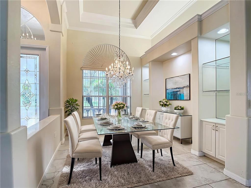 A formal dining room features a glass-topped table, crystal chandelier, and high tray ceilings — 18065 WING AVENUE, PORT CHARLOTTE, FL