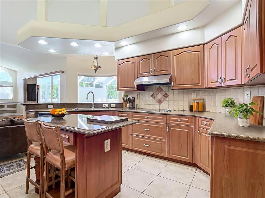 A kitchen features wood cabinets, a granite-topped island with two chairs, and tile flooring — 18065 WING AVENUE, PORT CHARLOTTE, FL