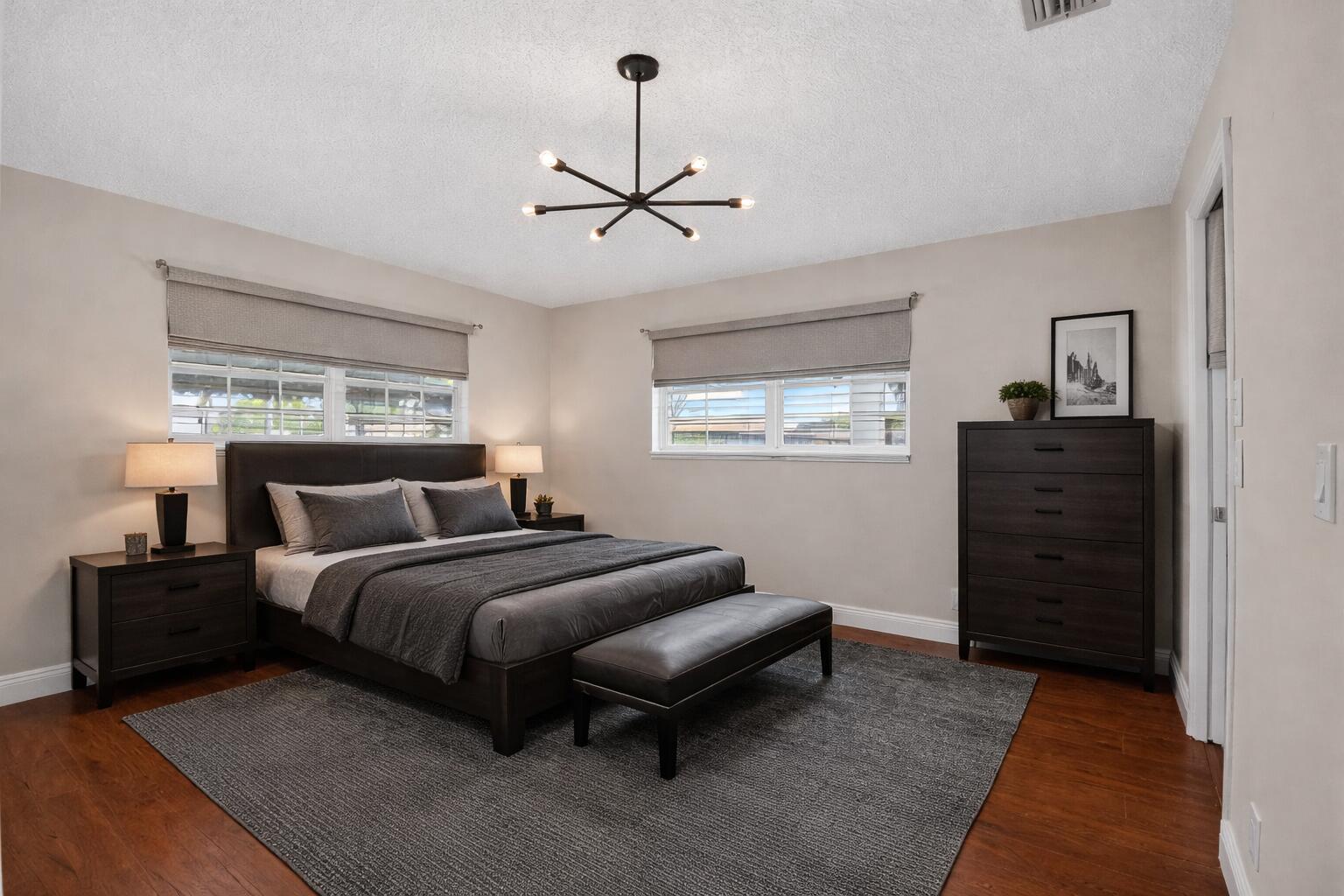 A bedroom with a dark wood bed, matching furniture, gray bedding, and a modern chandelier — 801 Meadowlark Lane, Delray Beach FL 33445, DELRAY BEACH, FL