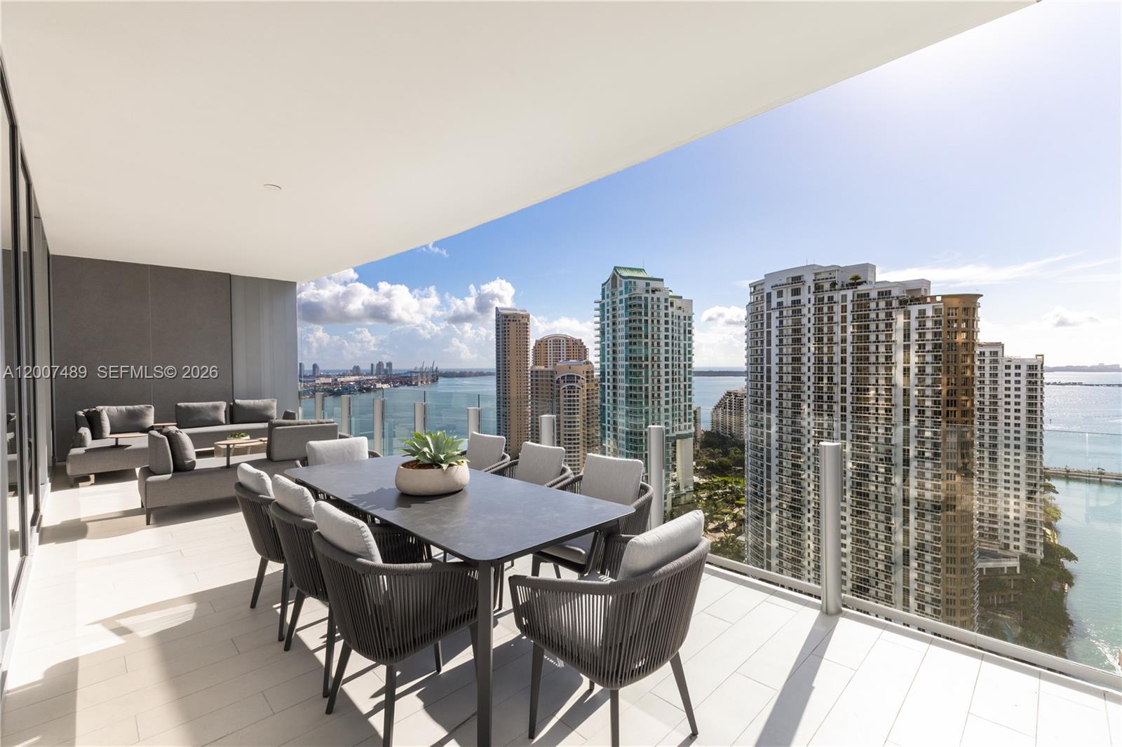A high-rise balcony features outdoor dining and lounge furniture overlooking a city skyline and bay — 300 Biscayne Blvd Way # 2802, Miami FL 33131, MIAMI, FL