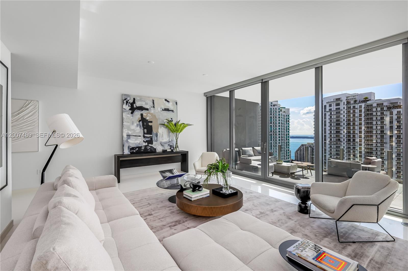 A modern living room features a white sofa, round coffee table, and floor-to-ceiling windows overlooking city buildings — 300 Biscayne Blvd Way # 2802, Miami FL 33131, MIAMI, FL