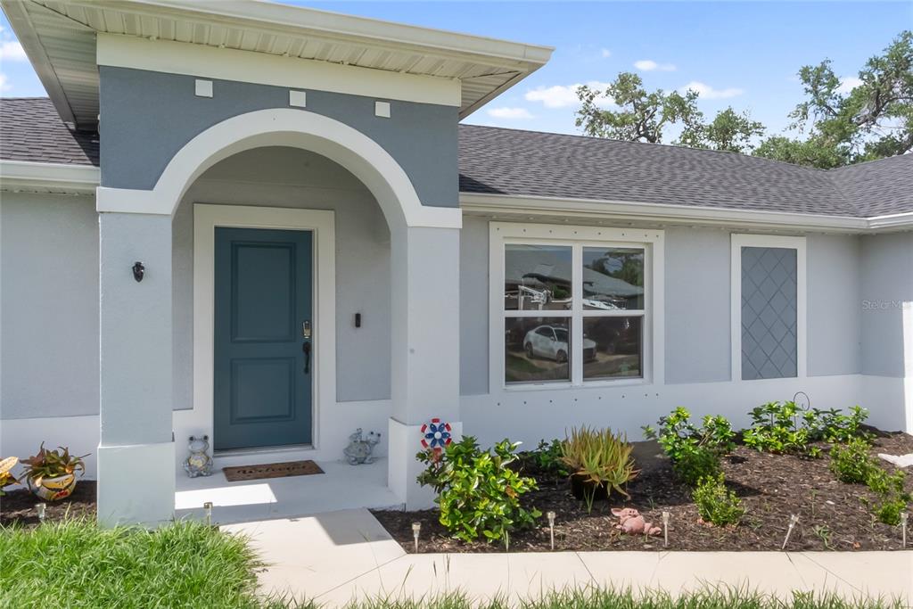 The exterior of a house features a blue front door, arched entryway, and landscaped garden — 3397 ZORATOA AVENUE, NORTH PORT, FL