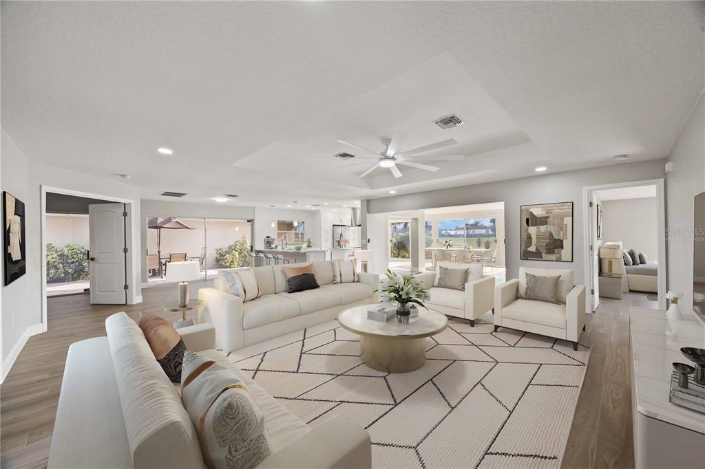 A bright, open-concept living room features a large sectional, white armchairs, and a geometric rug — 717 CARNOUSTIE TERRACE UNIT 9, VENICE, FL