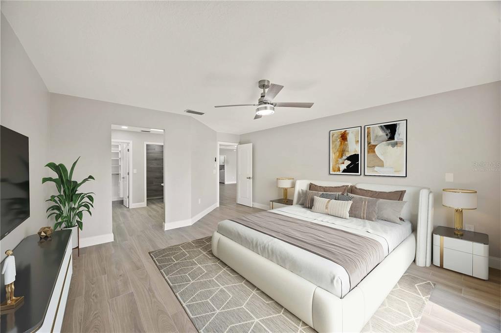 A bedroom features a white upholstered bed, gray wood-look flooring, and a ceiling fan — 717 CARNOUSTIE TERRACE UNIT 9, VENICE, FL