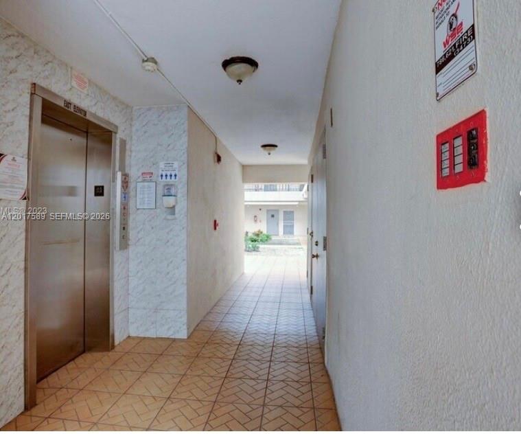 A hallway with tiled flooring leads to an elevator and an outdoor courtyard area — 5501 NW 7th St # E412, Miami FL 33126, MIAMI, FL