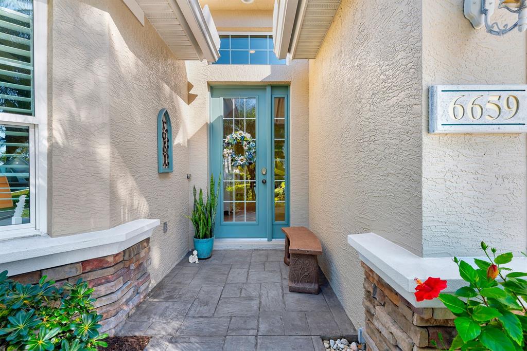 A teal front door with a wreath sits on a stone-paved entryway porch — 6659 PEBBLE BEACH WAY, LAKEWOOD RANCH, FL