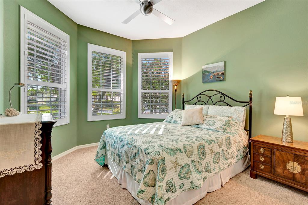 A bedroom with green walls, a seashell-patterned bedspread, and three windows with white shutters — 6659 PEBBLE BEACH WAY, LAKEWOOD RANCH, FL