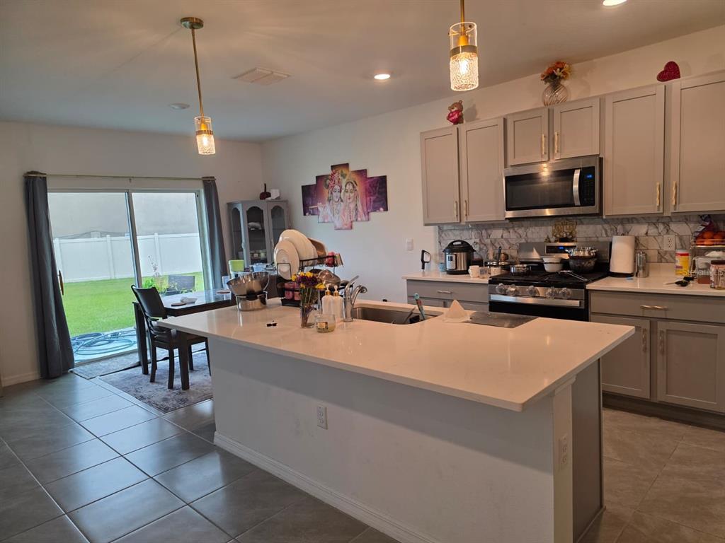 A kitchen with a large island, grey cabinets, stainless steel appliances, and a dining area — 35518 LOCKMAN WAY, ZEPHYRHILLS, FL