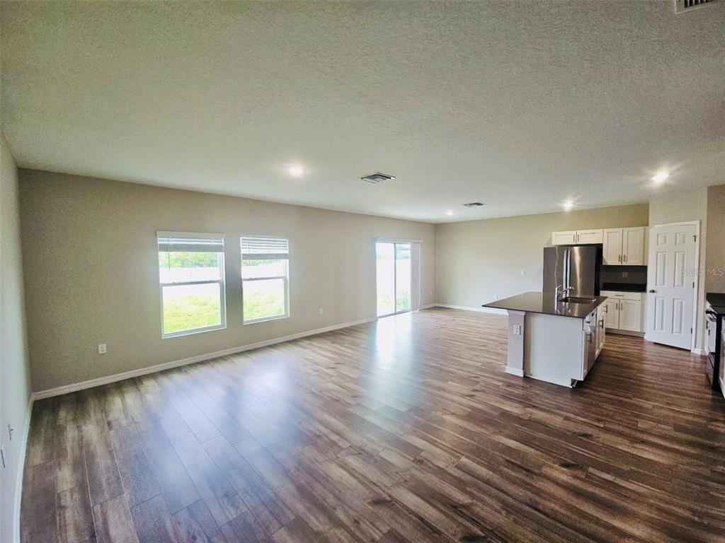 An open-concept living area with wood-look flooring, a kitchen island, and sliding glass doors — 34436 MOONFLOWER AVENUE, WESLEY CHAPEL, FL
