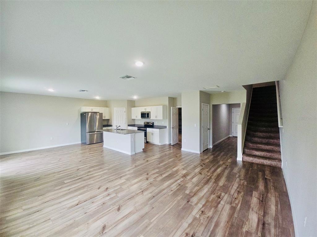 An open-concept kitchen and living area features white cabinets, stainless appliances, and wood-look flooring — 34436 MOONFLOWER AVENUE, WESLEY CHAPEL, FL
