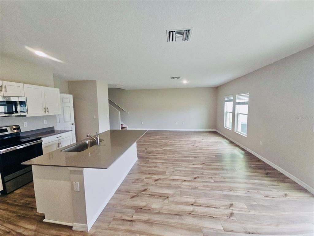 An open-concept kitchen with a quartz island and wood-look flooring leads into a living area — 34436 MOONFLOWER AVENUE, WESLEY CHAPEL, FL