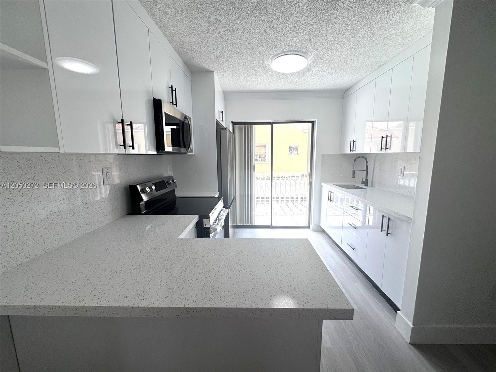 A modern kitchen features white cabinets, speckled countertops, and a sliding glass door — 2740 W 62nd St # 205, Hialeah FL 33016, HIALEAH, FL
