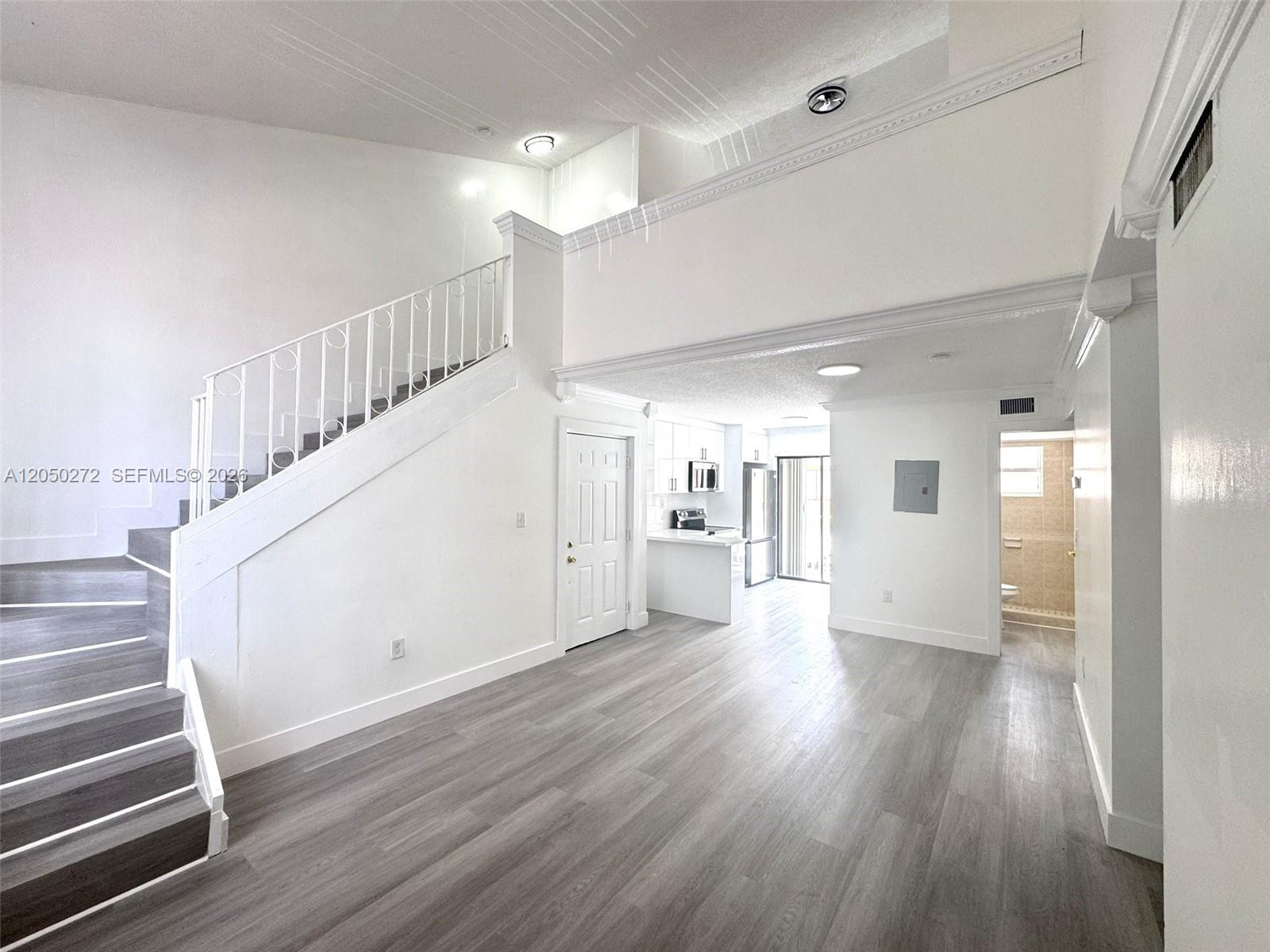 A bright living area features wood-look flooring, a staircase with white railings, and an open kitchen — 2740 W 62nd St # 205, Hialeah FL 33016, HIALEAH, FL
