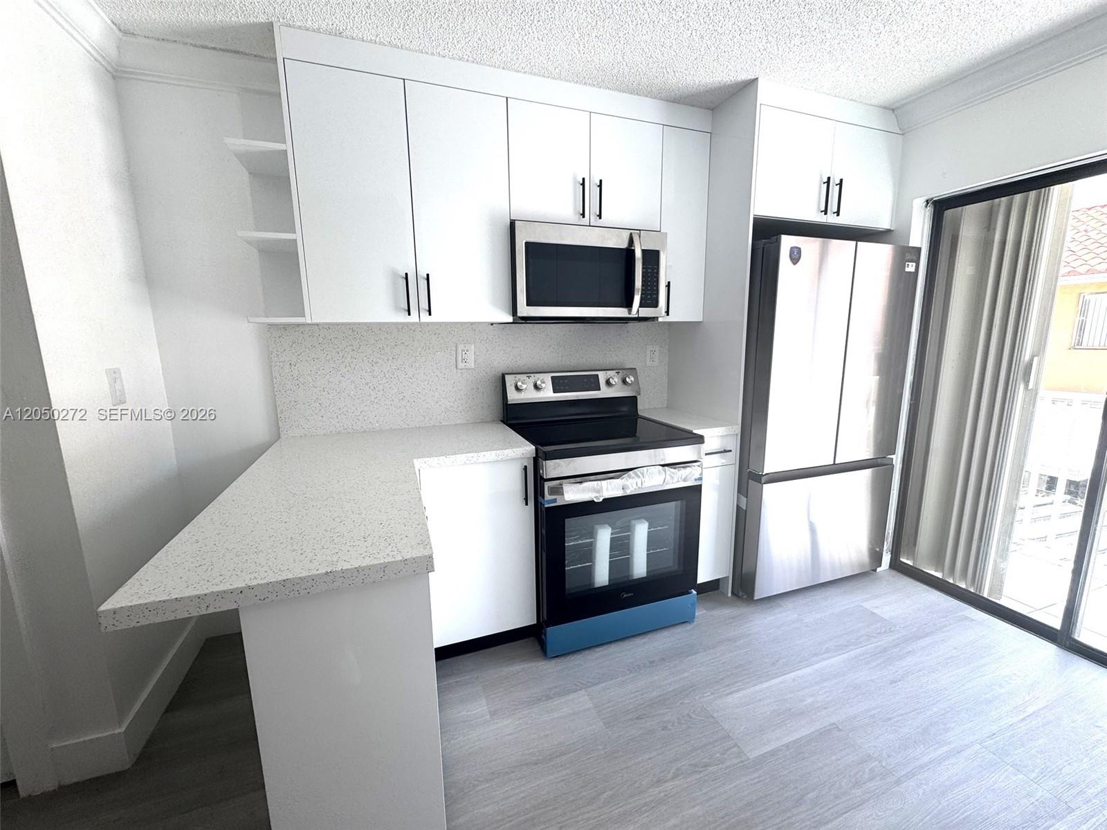 A modern kitchen features white cabinetry, stainless steel appliances, and light speckled countertops — 2740 W 62nd St # 205, Hialeah FL 33016, HIALEAH, FL