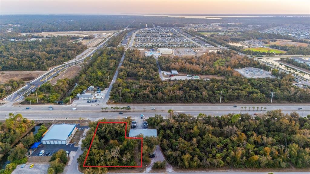 An aerial view shows a vacant, wooded lot outlined in red next to commercial buildings — 732 TAMIAMI TRAIL, PORT CHARLOTTE, FL