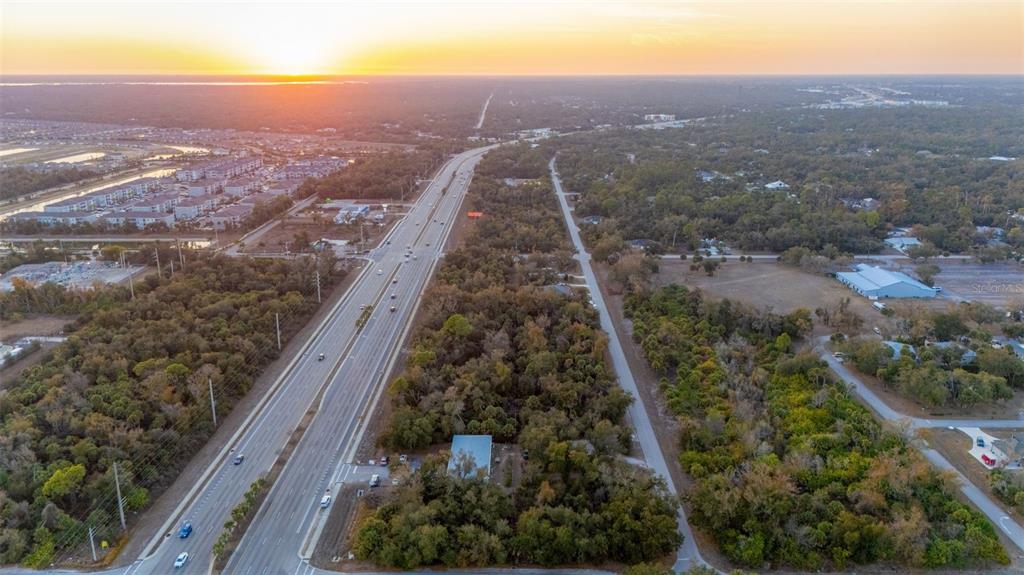 An aerial view shows a multi-lane highway running alongside a wooded lot with a house — 732 TAMIAMI TRAIL, PORT CHARLOTTE, FL