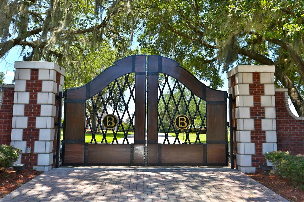 A large arched wooden and metal gate with a letter B emblem stands between brick pillars — 6800 & 6500 NW 193RD STREET, MICANOPY, FL