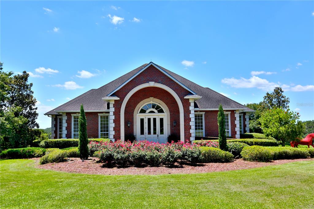 A brick house with a prominent arched entryway and landscaped garden under a blue sky — 6800 & 6500 NW 193RD STREET, MICANOPY, FL