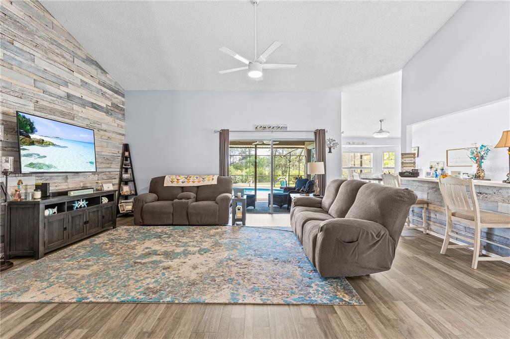 A living room features a wood-paneled accent wall, a large area rug, and sliding glass doors — 13007 TITLEIST DRIVE, HUDSON, FL