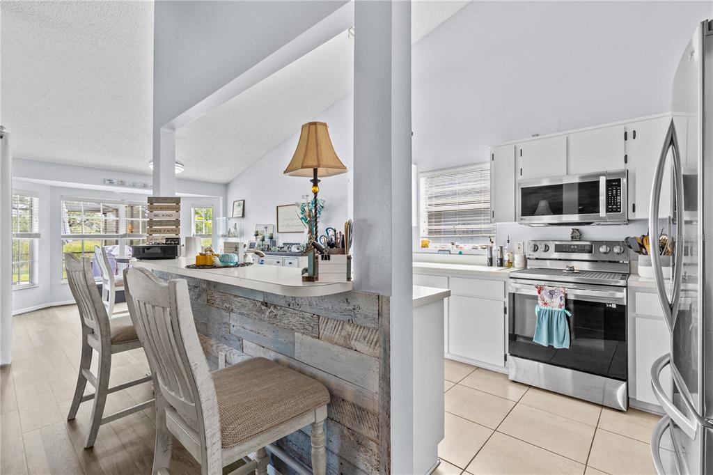 A kitchen with white cabinets and stainless steel appliances overlooks a dining area with bar seating — 13007 TITLEIST DRIVE, HUDSON, FL