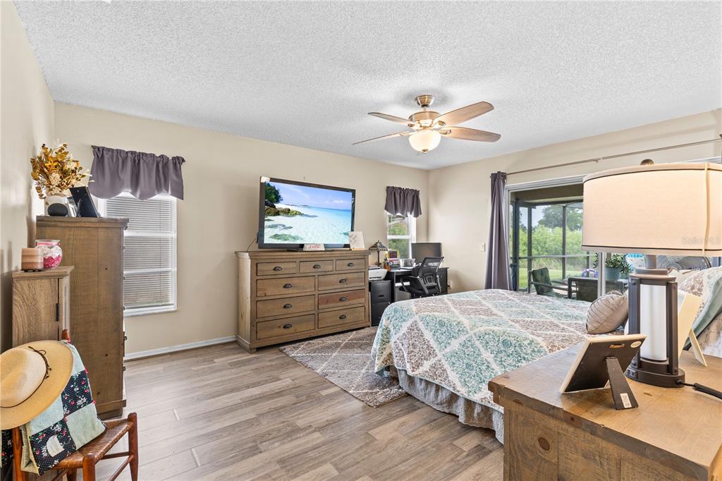 A bedroom features wood-look flooring, a ceiling fan, a dresser with a television, and a bed — 13007 TITLEIST DRIVE, HUDSON, FL