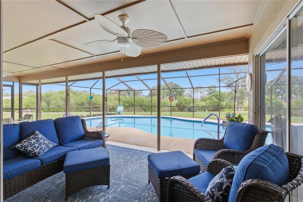 A covered patio with wicker furniture overlooks a screened-in swimming pool and backyard — 13007 TITLEIST DRIVE, HUDSON, FL
