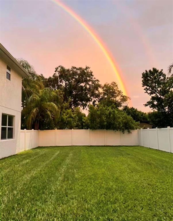 A backyard with a green lawn, white vinyl fence, and a rainbow in the sky — 3008 E SLIGH AVENUE, TAMPA, FL