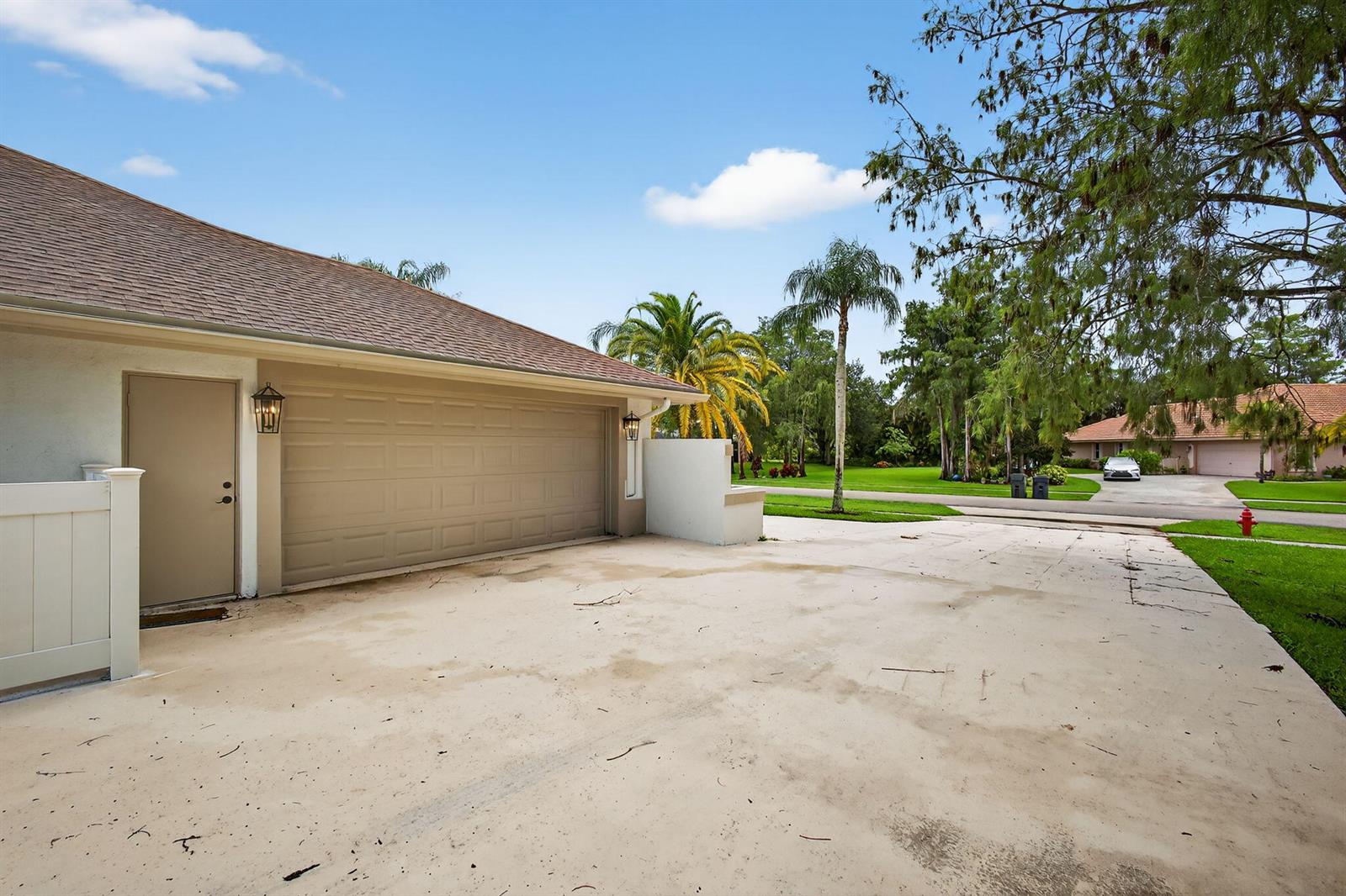A beige garage door and side door face a concrete driveway under a blue sky — 1295 Longlea Terrace, Wellington FL 33414, WELLINGTON, FL