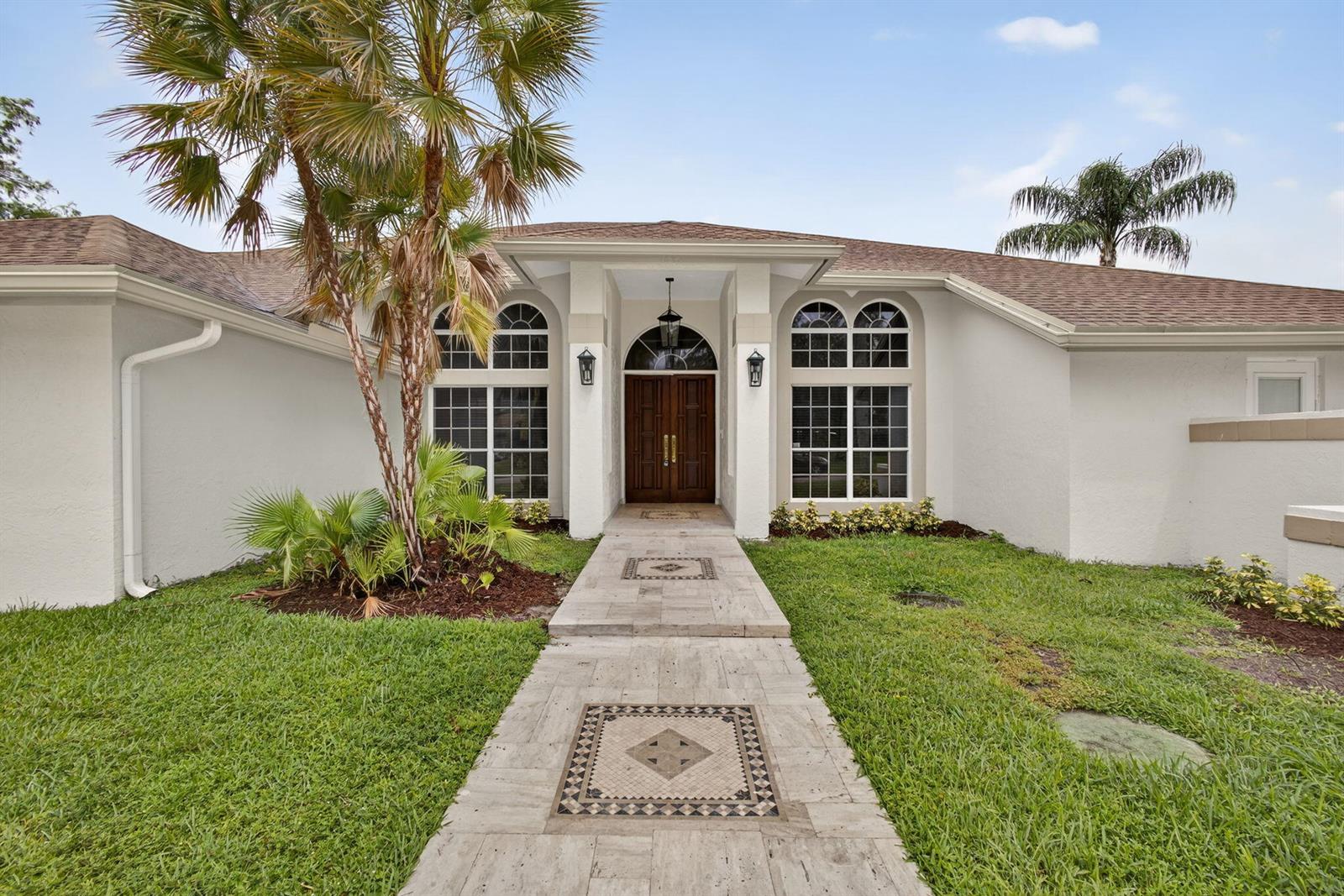 A single-story house with a white exterior, arched windows, and a stone walkway leading to double doors — 1295 Longlea Terrace, Wellington FL 33414, WELLINGTON, FL