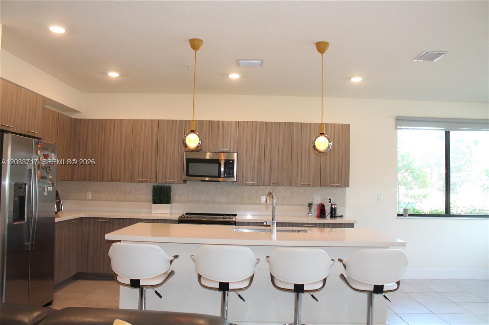 A modern kitchen features wood-grain cabinets, a white island with four stools, and pendant lighting — 8265 NW 41 ST # 110, Doral FL 33166, DORAL, FL